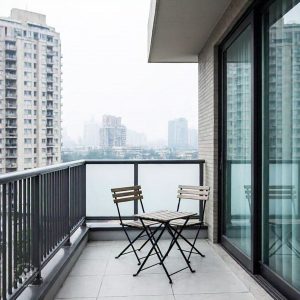 A modern home balcony design featuring a cozy seating area with cushioned chairs and a small coffee table, surrounded by lush green plants and soft ambient lighting