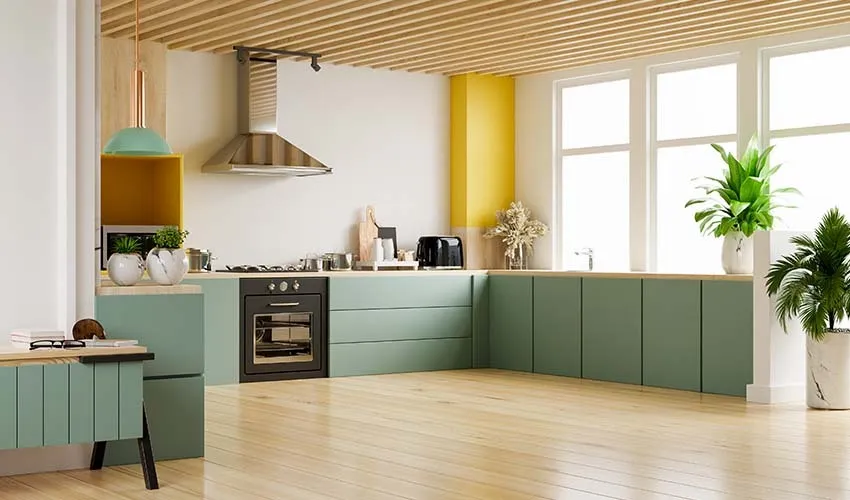 Modern Scandinavian-style L-shaped kitchen with muted green cabinets, a wooden ceiling, large windows for natural light, and minimalist décor featuring plants and pendant lighting.