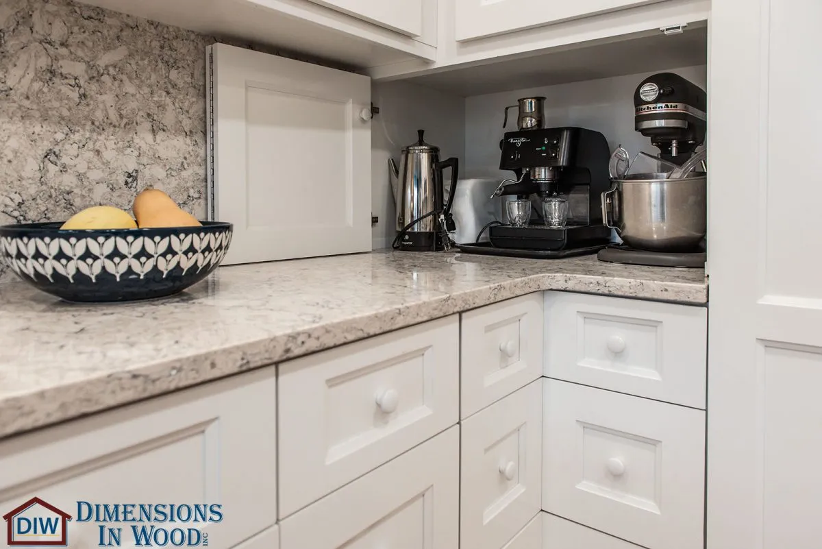 Luxury L-shaped kitchen interior with white cabinetry, marble countertops, built-in appliance storage, and an organized coffee station.