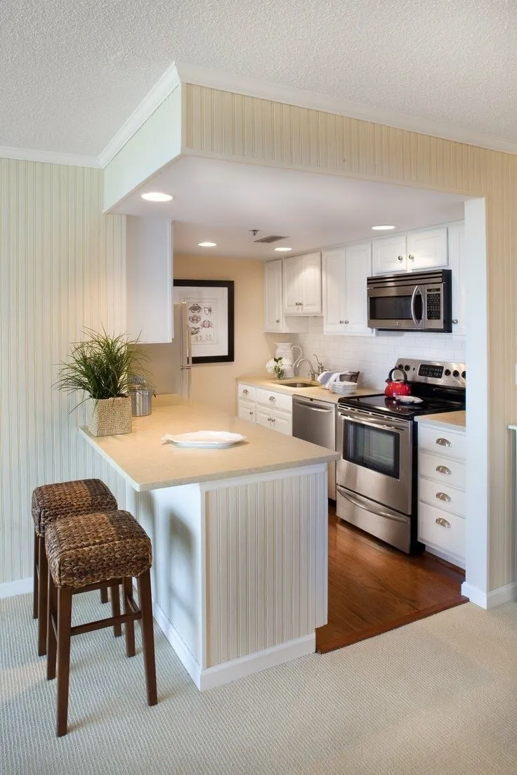 Compact open kitchen with white cabinets, beige counters, and bar stools.