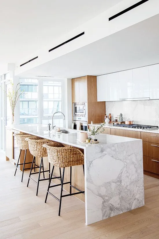 Modern open kitchen with marble island, wood cabinets, and wicker stools.