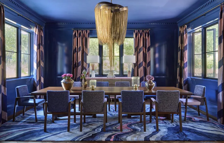 Luxurious navy blue dining room with gold chandelier and wood table.