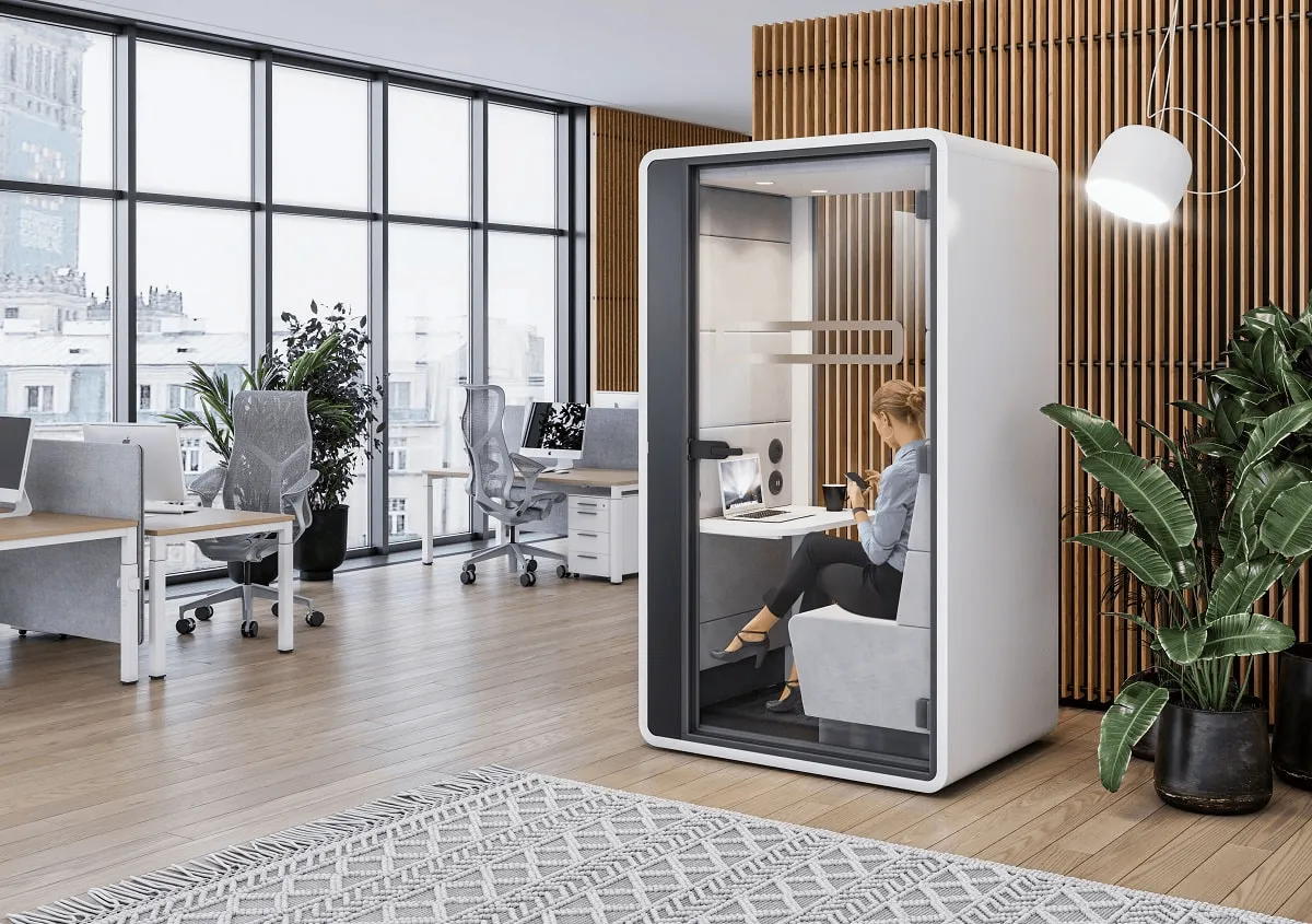 Office pod in co-working space with desks and plants.