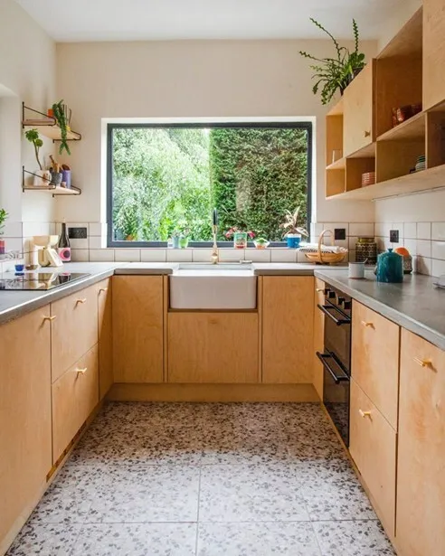 Compact kitchen interior, wood cabinets, plants, window view.